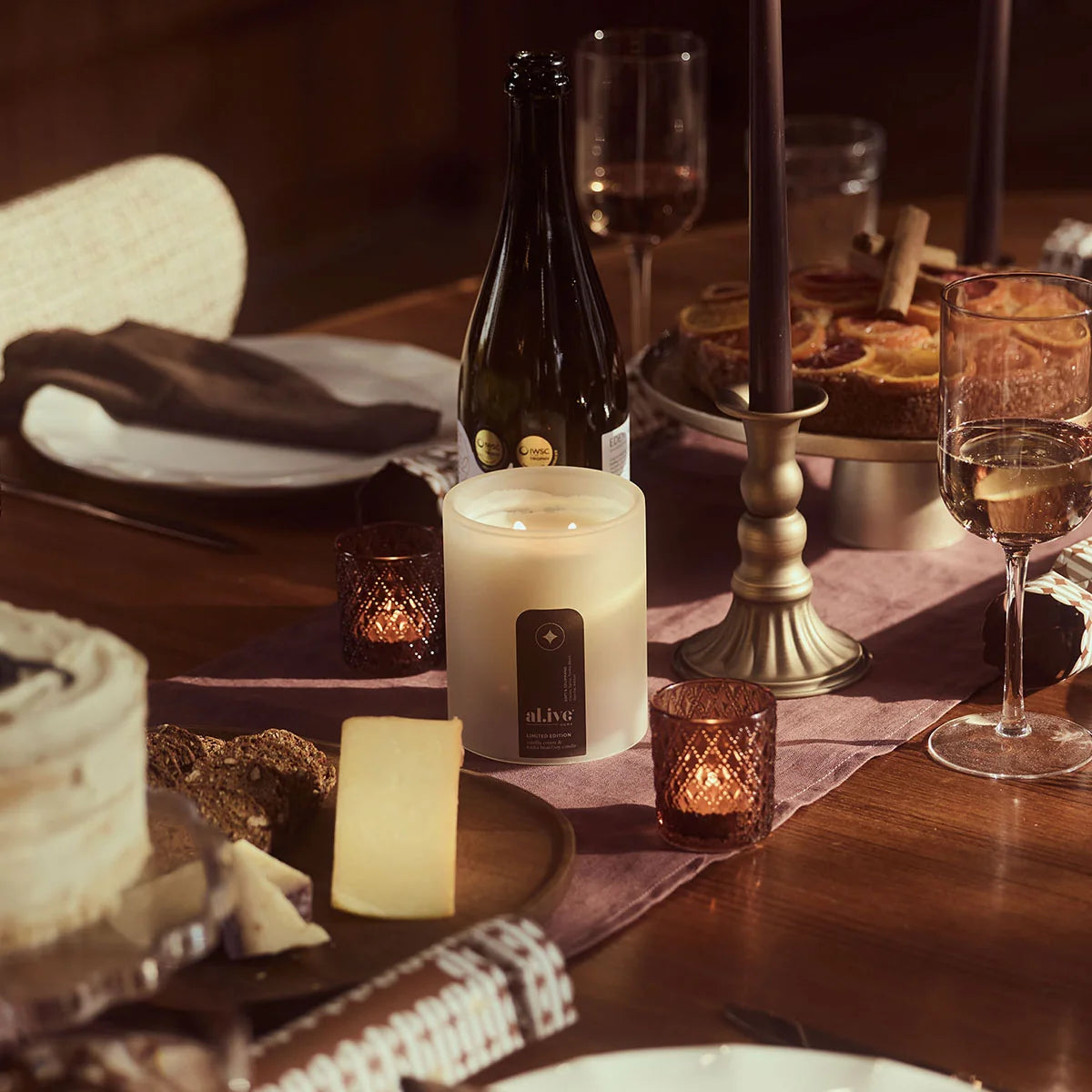 al.ive body Vanilla Cream & Tonka Bean Soy Candle glowing on a Christmas dinner table