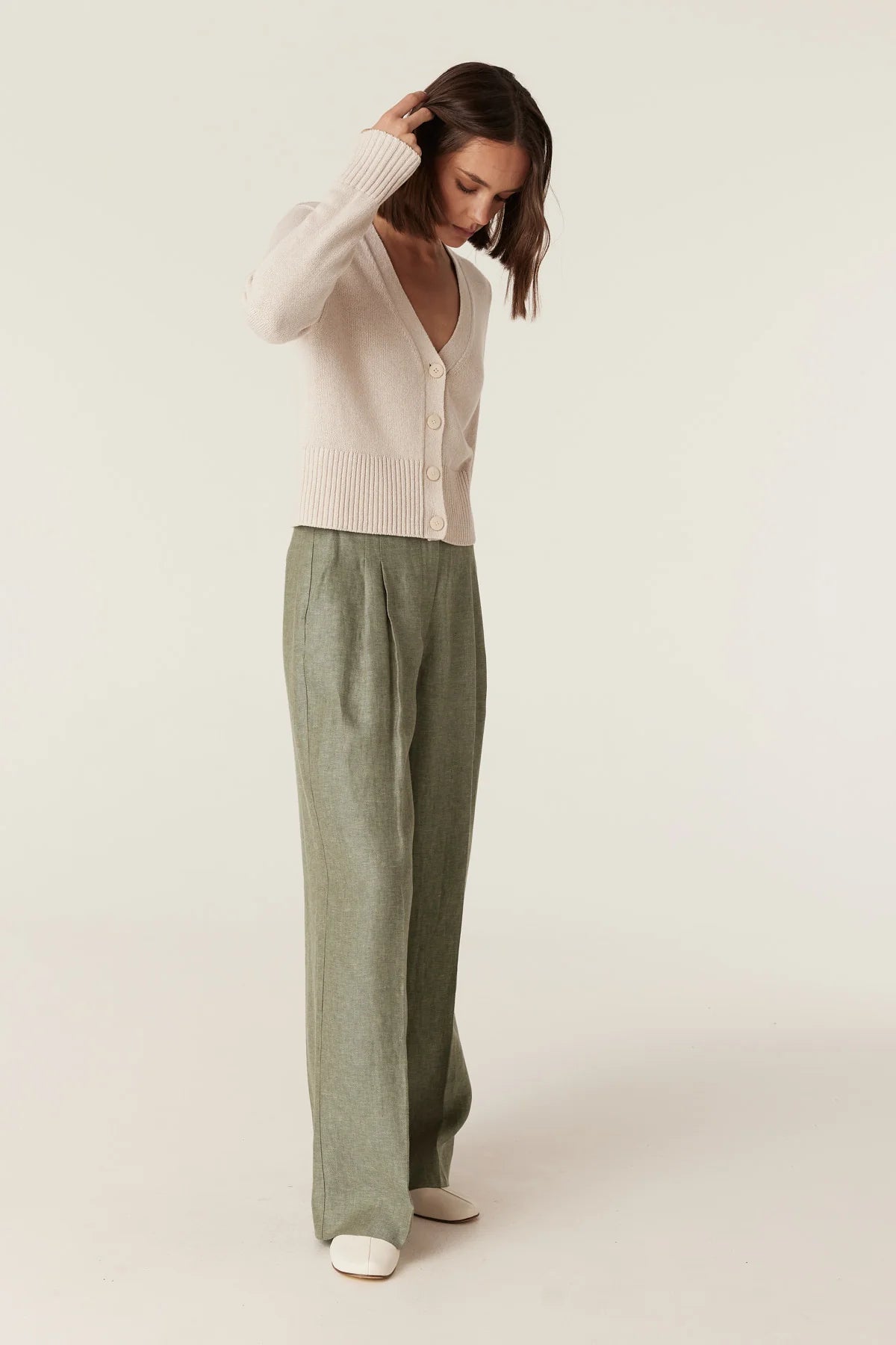 Cable Melbourne Evelyn Linen Pant in Green, worn - side view, styled with a cream cardigan (not included)