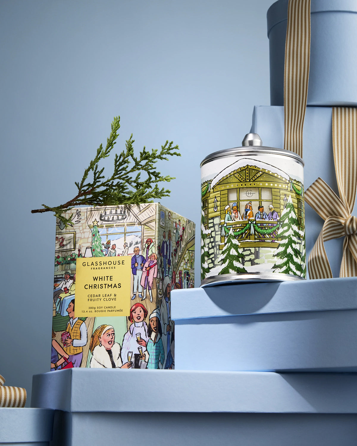 Glasshouse Fragrances White Christmas 380g Candle and box styled on blue gift boxes with cedar sprig